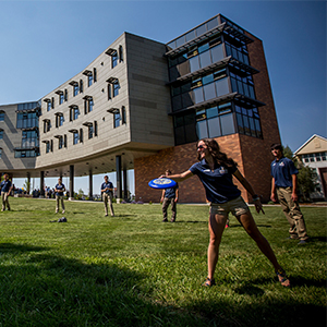 Students throwing a frisbee in front of Yellowstone Hall in summer.